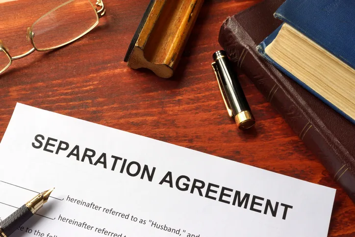 A separation agreement document on a desk with a pen, open book, and reading glasses case nearby.