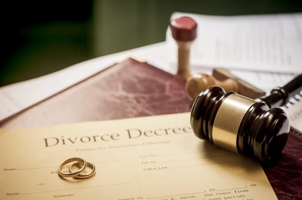 A divorce decree form, two wedding rings, a judge’s gavel, and legal documents arranged on a desk.