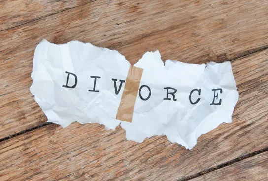 A torn piece of paper with the word “DIVORCE” taped together sits on a wooden surface.